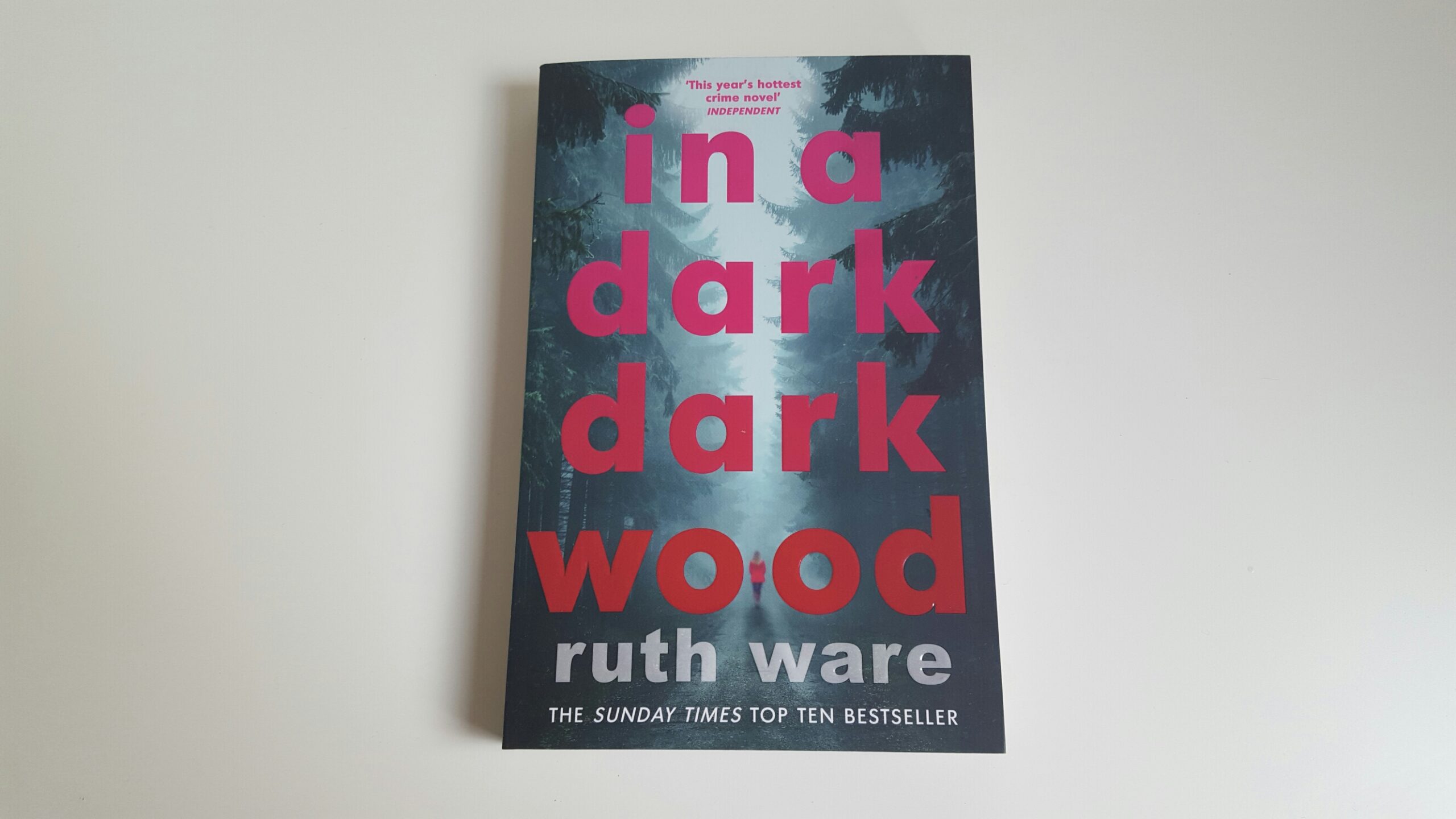 In a Dark, Dark Wood by Ruth Ware. The cover shows a silhouette of a woman walking in a forest that is engulfed in fog. The title of the book is written in a pink to red gradient color.