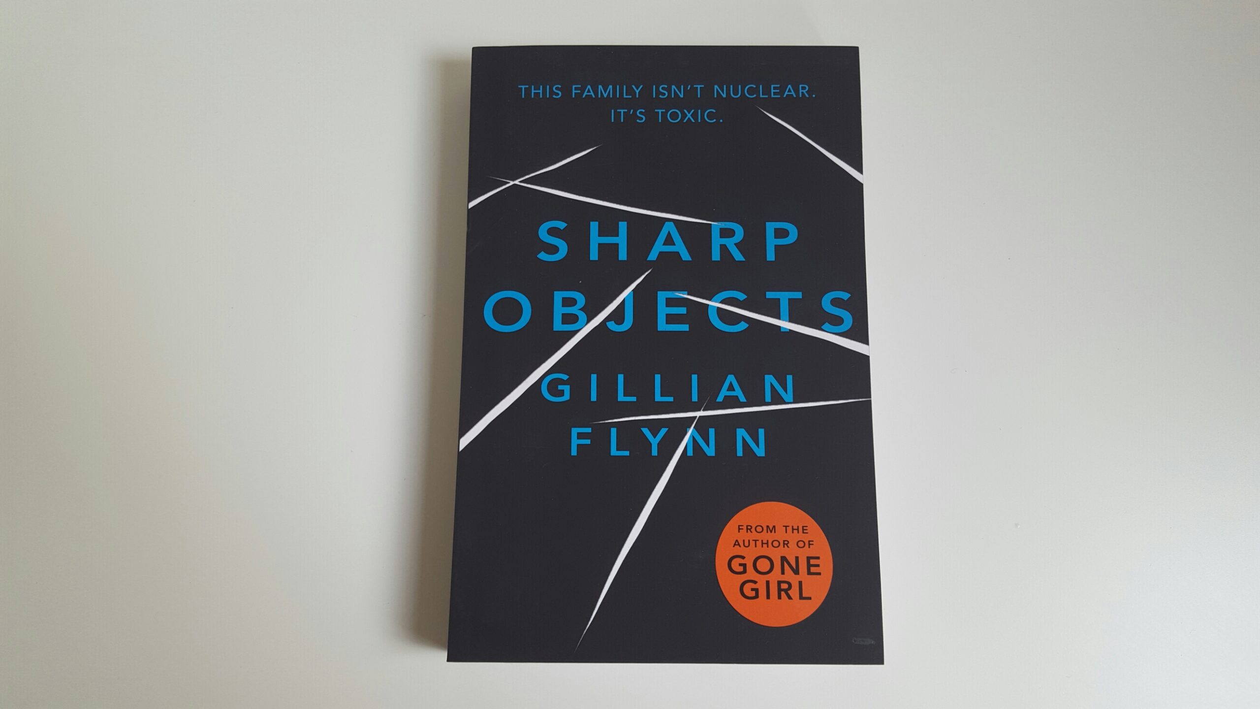 Sharp Objects by Gillian Flynn. The book has a black cover with white marks that appear as cuts. The title of the book is written in a blue font.