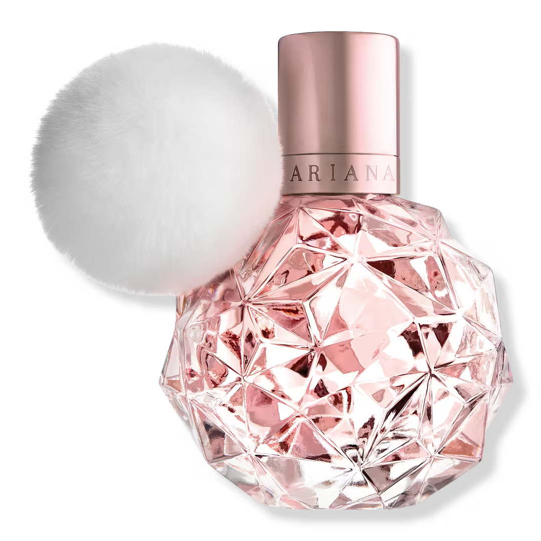 The Ari by Ariana Grande perfume which is in a light pink glass bottle with a geometric design. The bottle also has a white fluffy ball attached to it.