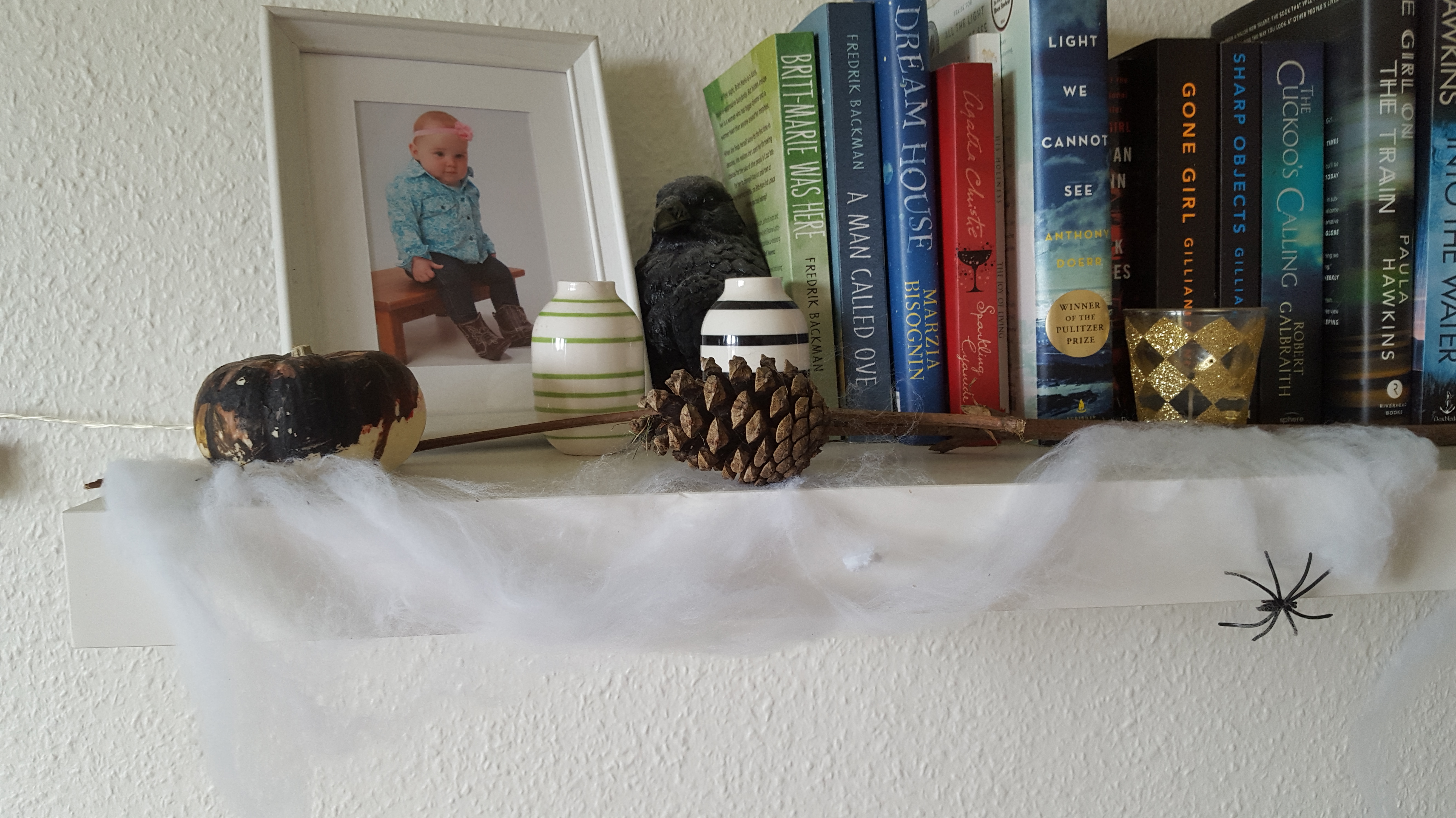 A small painted pumpkin, pine cone, twig, and cotton spider's web on a shelf