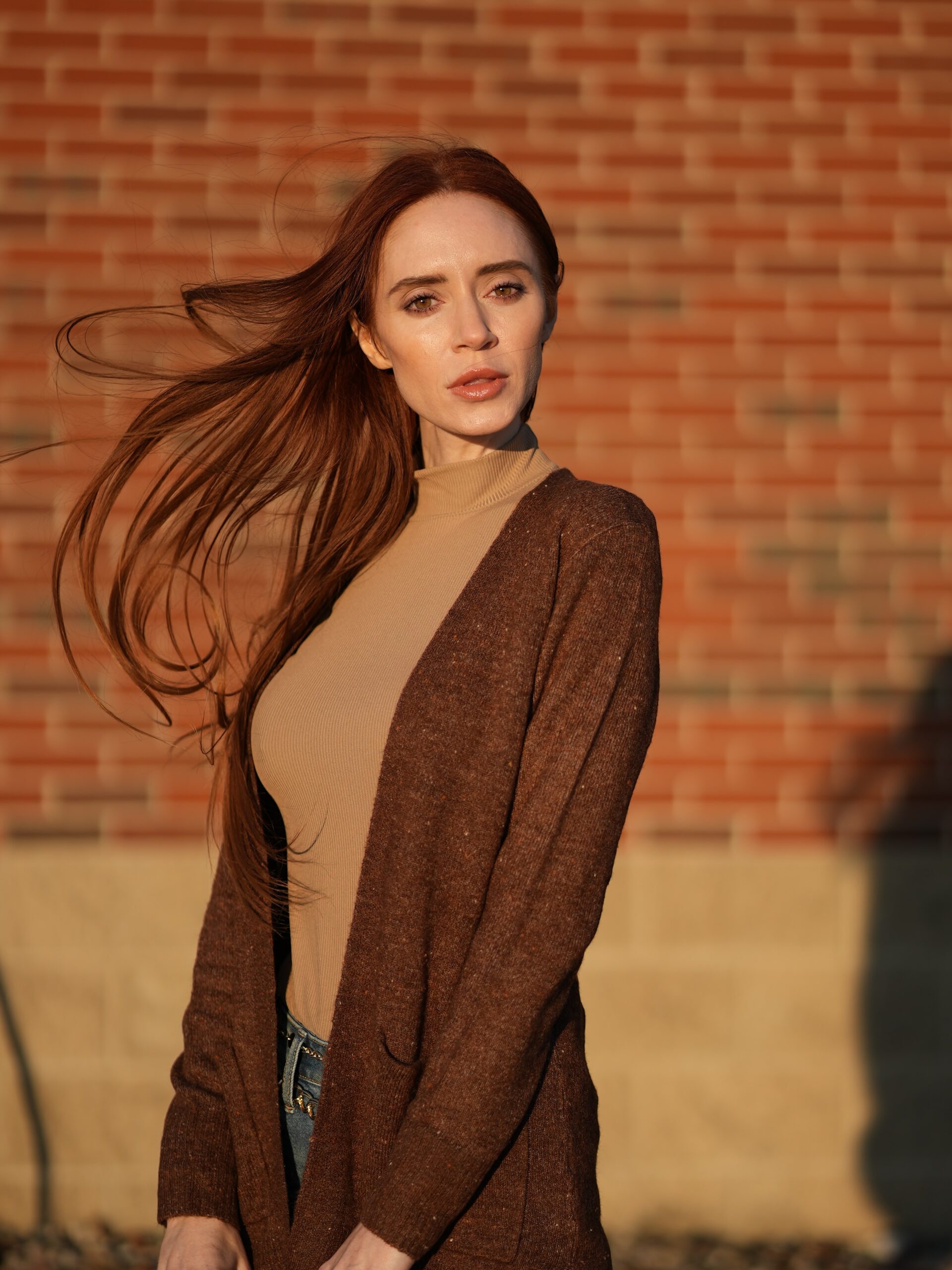 A woman wearing a light brown shirt and a brown cardigan. 