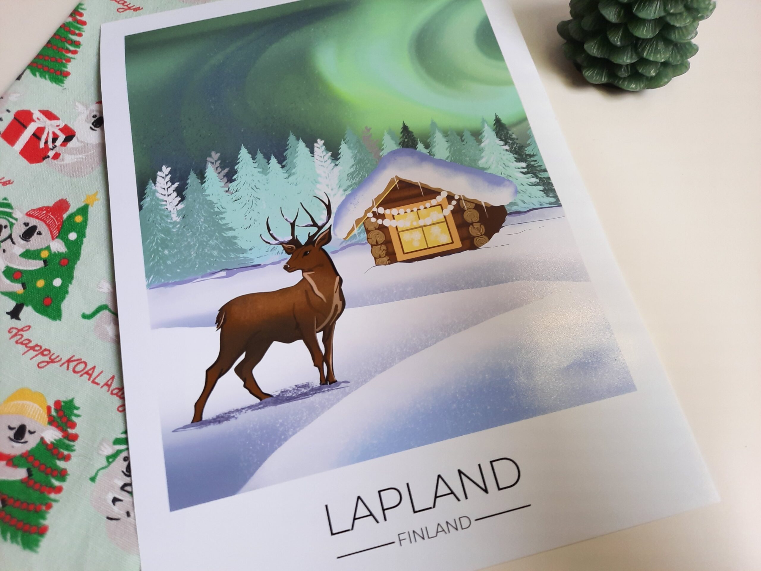 The Lapland poster from Dreamers who Travel that depicts a deer in front of a log cabin in the snow and the Northern Lights in the background