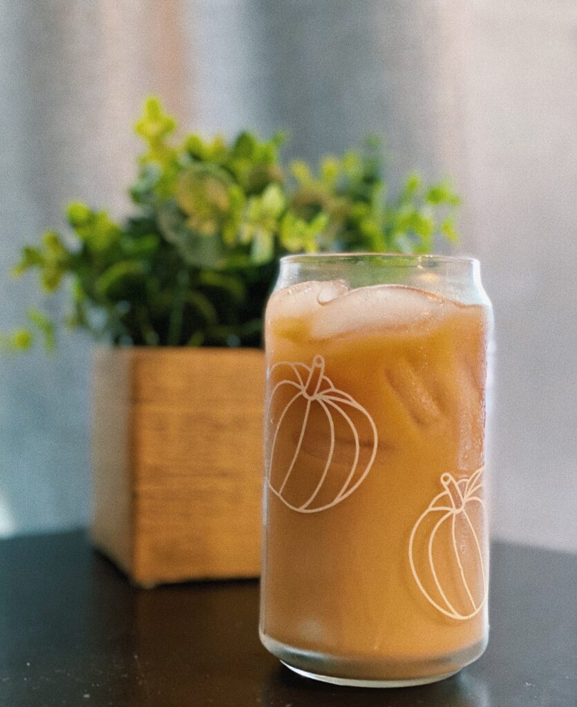 A beer can shaped glass that has a pumpkin design and is filled with iced coffee