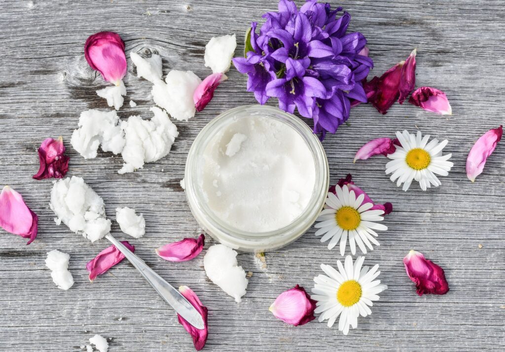 An opened jar of coconut oil that is surrounded by rose petals and daisies.
