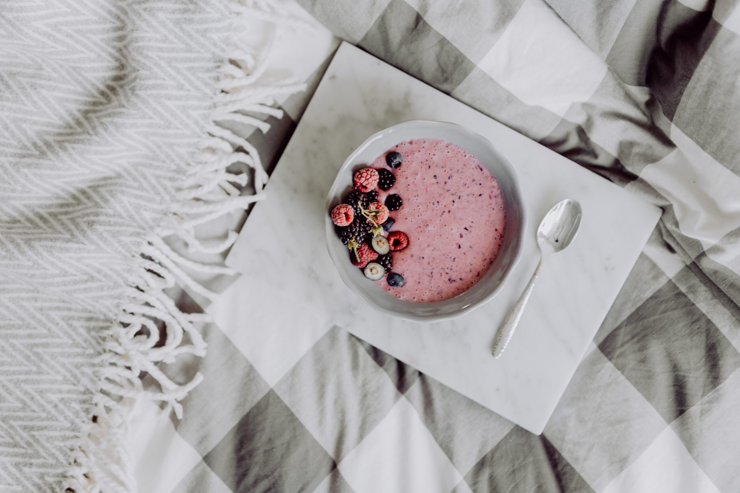 A bowl of yogurt with fresh berries that appears to be laying on a grey plaid blanket.