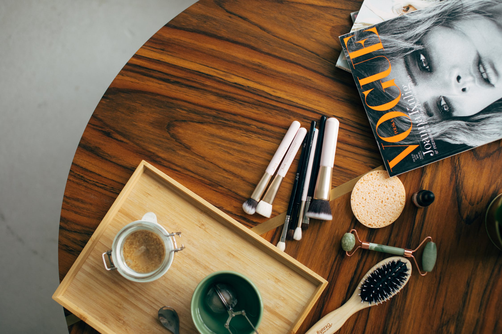 A table that has an issue of Vogue magazine and makeup brushes and tools on it. The media is one factor that can affect body iamge.