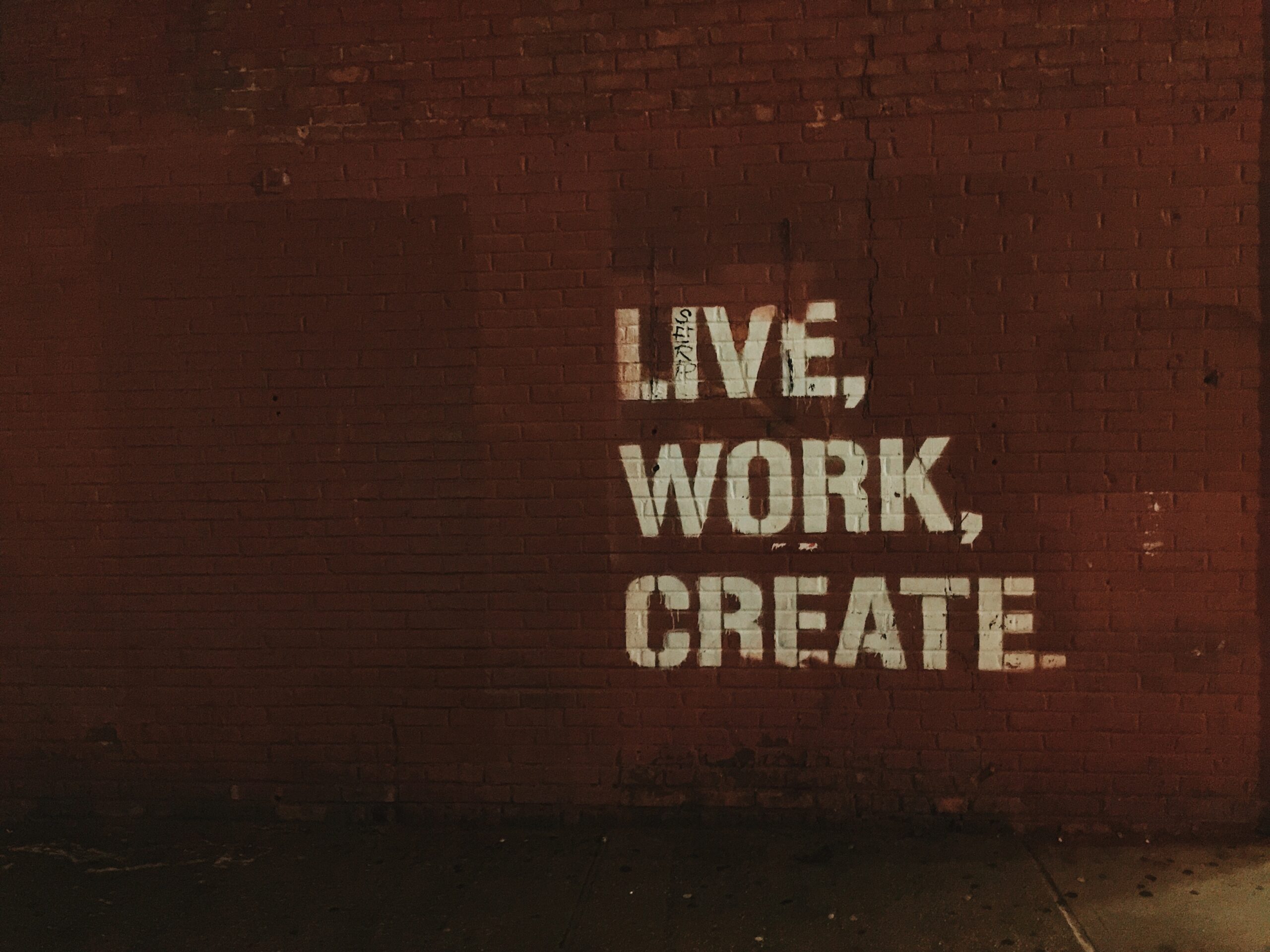 Graffiti on a red brick wall that states live, work, create