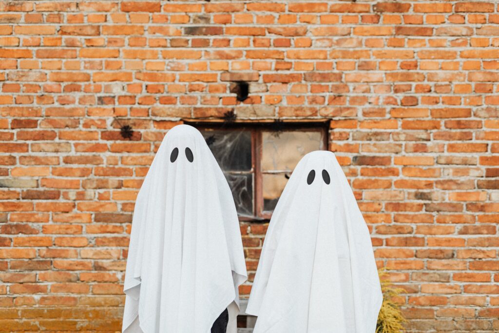 Two people in ghost sheet costumes standing in front of a brick wall, which is a good idea for a sustainable Halloween costume