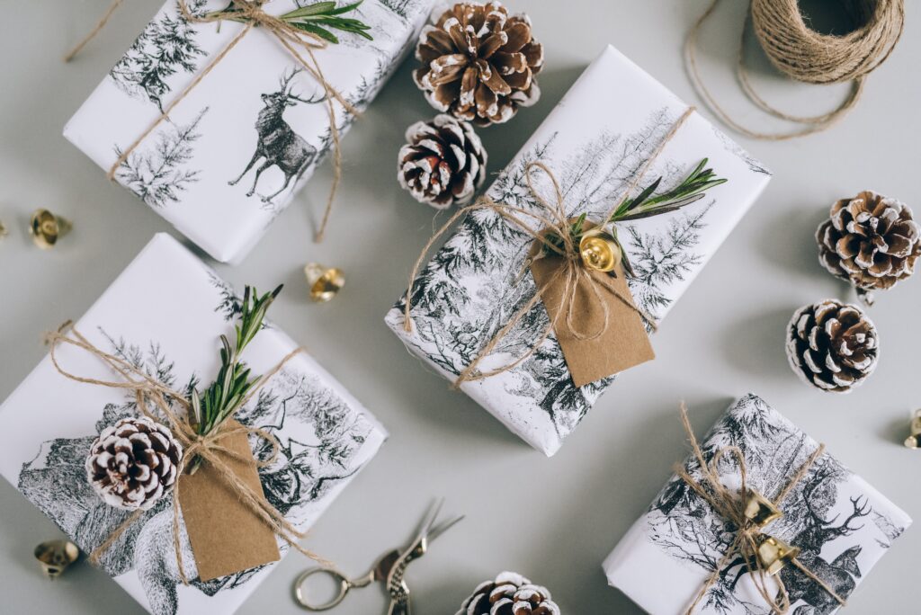 4 Christmas presents wrapped in a Christmas-themed wrapping paper with deer and snow-covered trees. The presents are wrapped with twine. 
