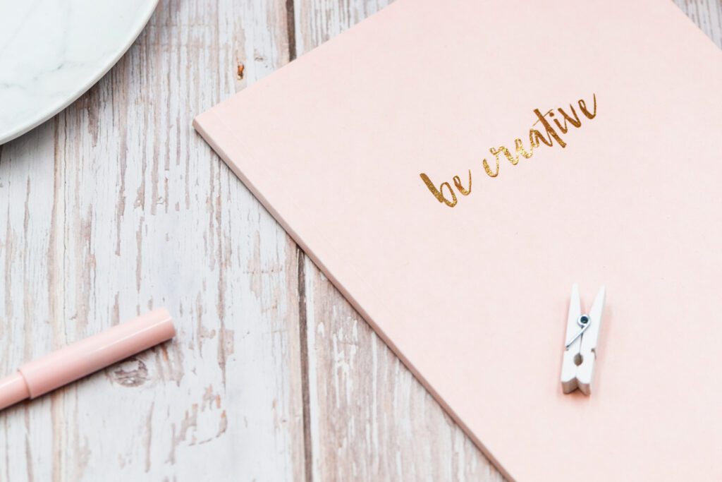 A close up of a pink notebook with the words be creative written in gold.