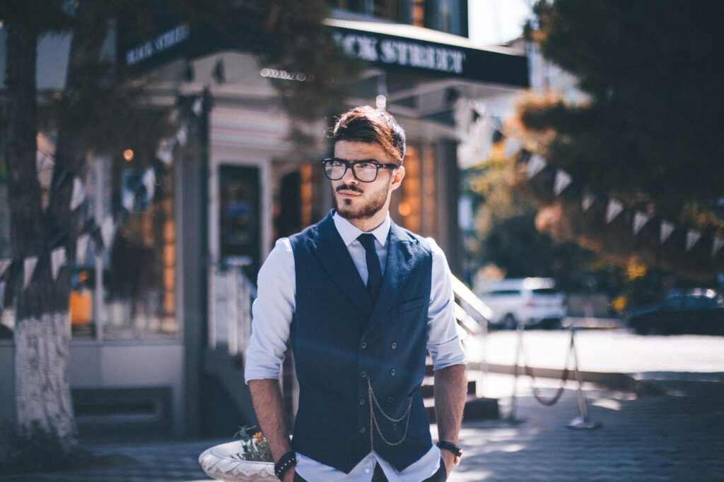 A man wearing a quarter length sleeved shirt, blue vest, and tie and looking sideways