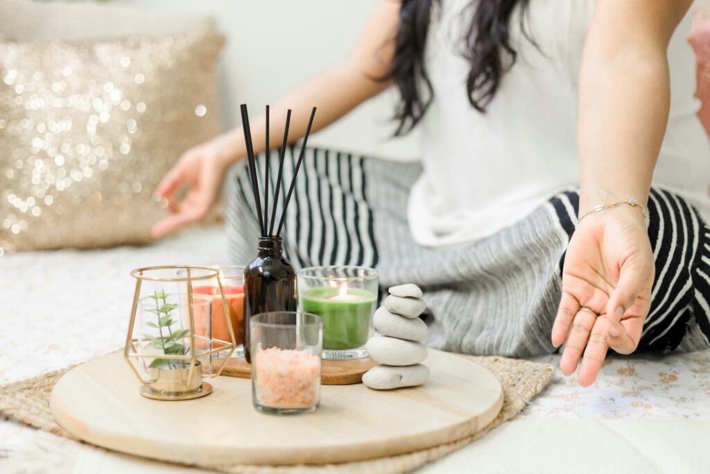 A woman in a white tank top meditating in front of a tray with incense and candles