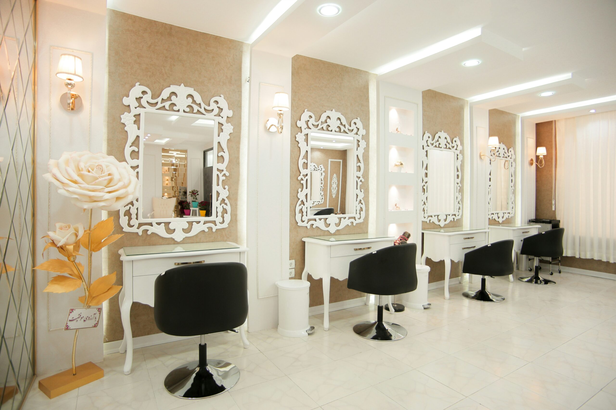 A salon with 4 black chairs facing ornate white mirrors