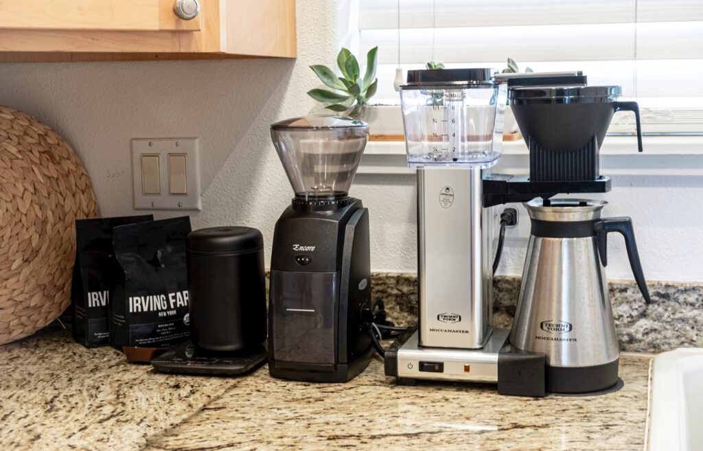 A grinder and coffee maker on a kitchen counter next to bags of coffee