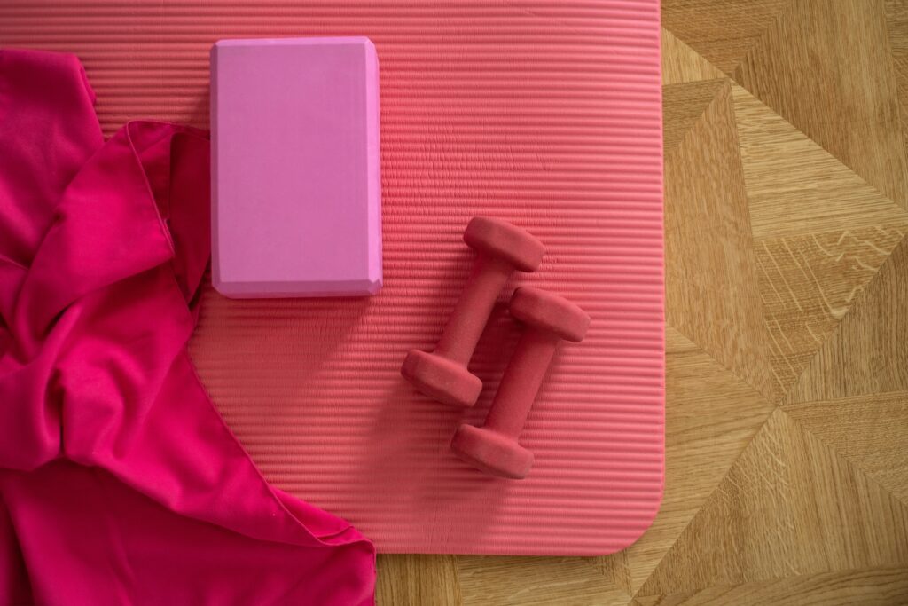A pink yoga mat that has pink dumbells and a block on top.