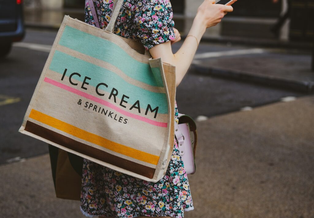 A canvas tote bag that says Ice Cream & Sprinkles on the side wth blue, pink, yellow, and brown stripes. Tote bags are a good option for handbags. 