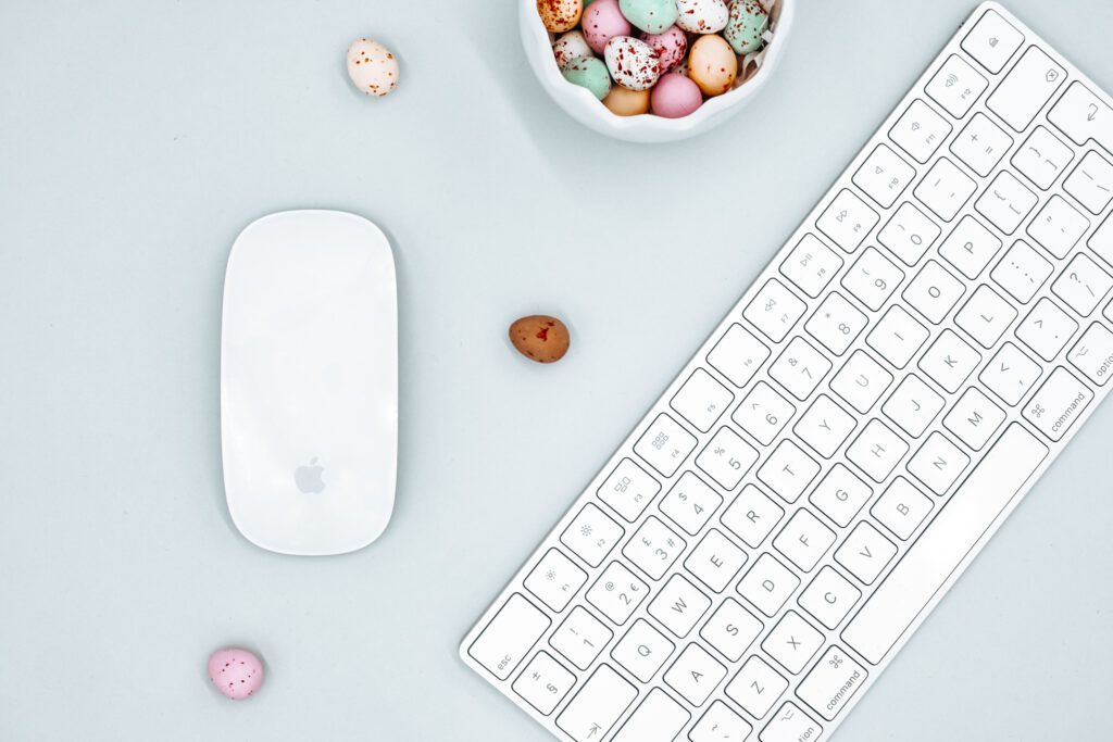 A white keyboard and mouse on a blank background. Next to the keyboard and mouse is a bowl filled with candy eggs.