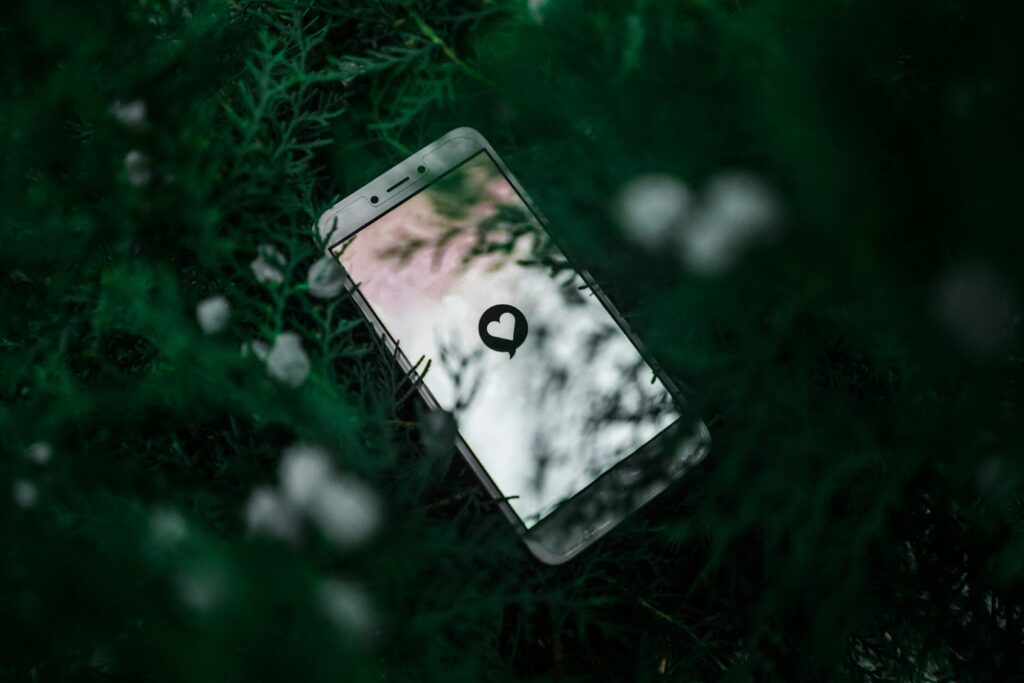 A phone with a white heart on the screen and green leaves in the background 