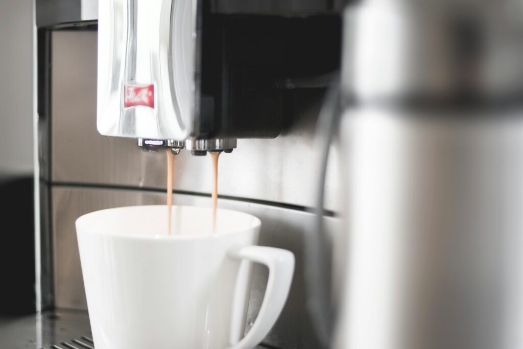 A coffee maker filling a white cup with cofee