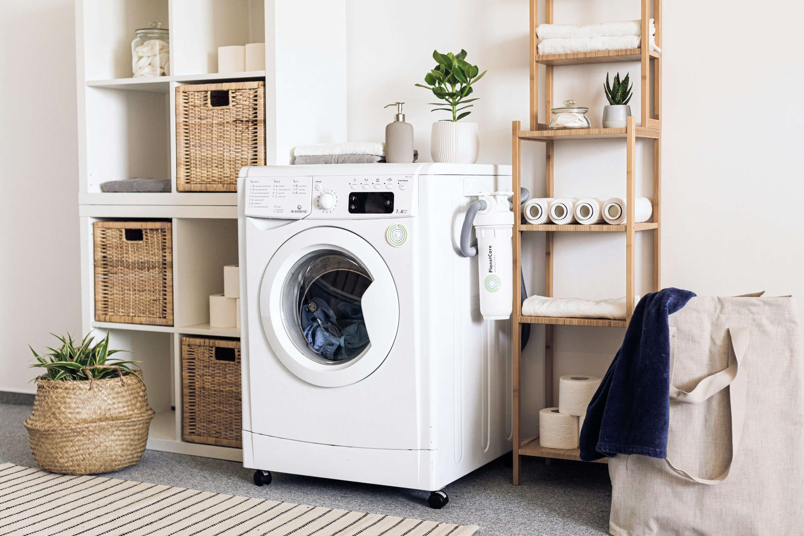 A dryer that is filled with clothes and next to shelves and a laundry basket