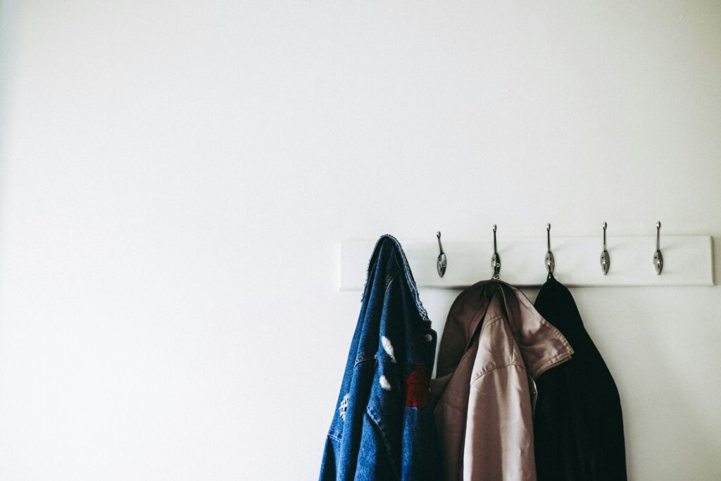 A white wall hook with 3 jackets hanging from them