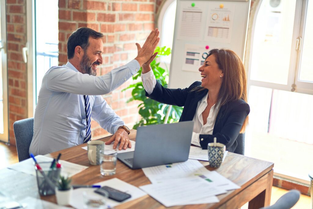 A man and woman smiling and high-fiving each other at work.