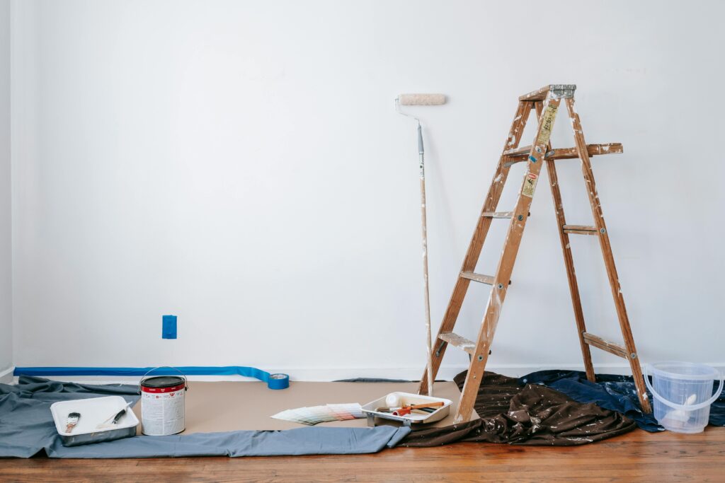 A ladder in a home with a paint roller and paint cans
