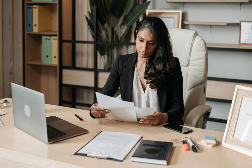 A female lawyer wearing a white shirt and black suit jacket sitting at a desk and looking at documents