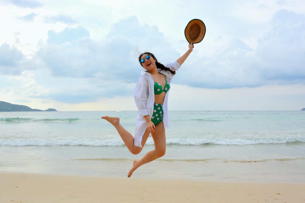 A woman wearing a green and white polka dot bikini with her hair tied in a braid while jumping on the beach