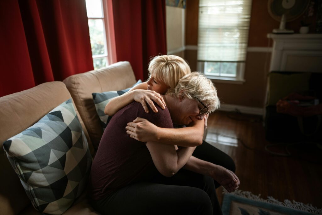 A young woman with blonde hair hugging an elderly woman on a couch
