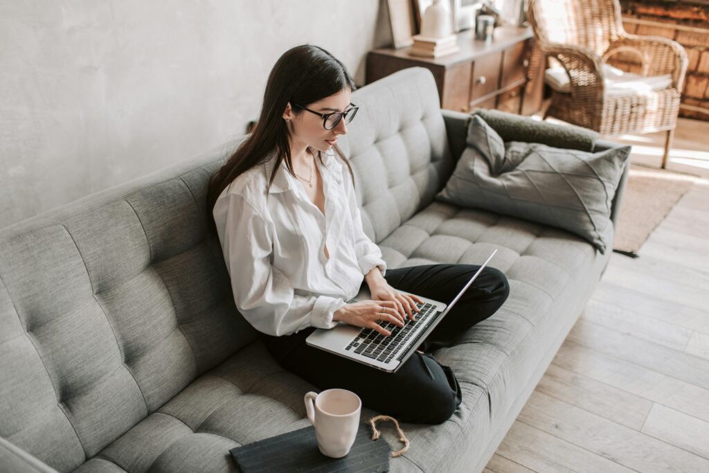 A woman sitting at home on a couch and working on her laptop
