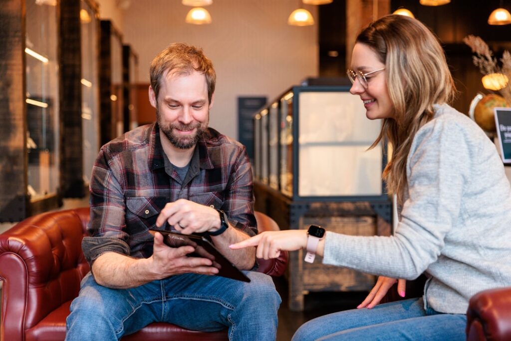 A man and woman at a coffee shop, intently looking at a tablet, surrounded by a cozy and inviting atmosphere.