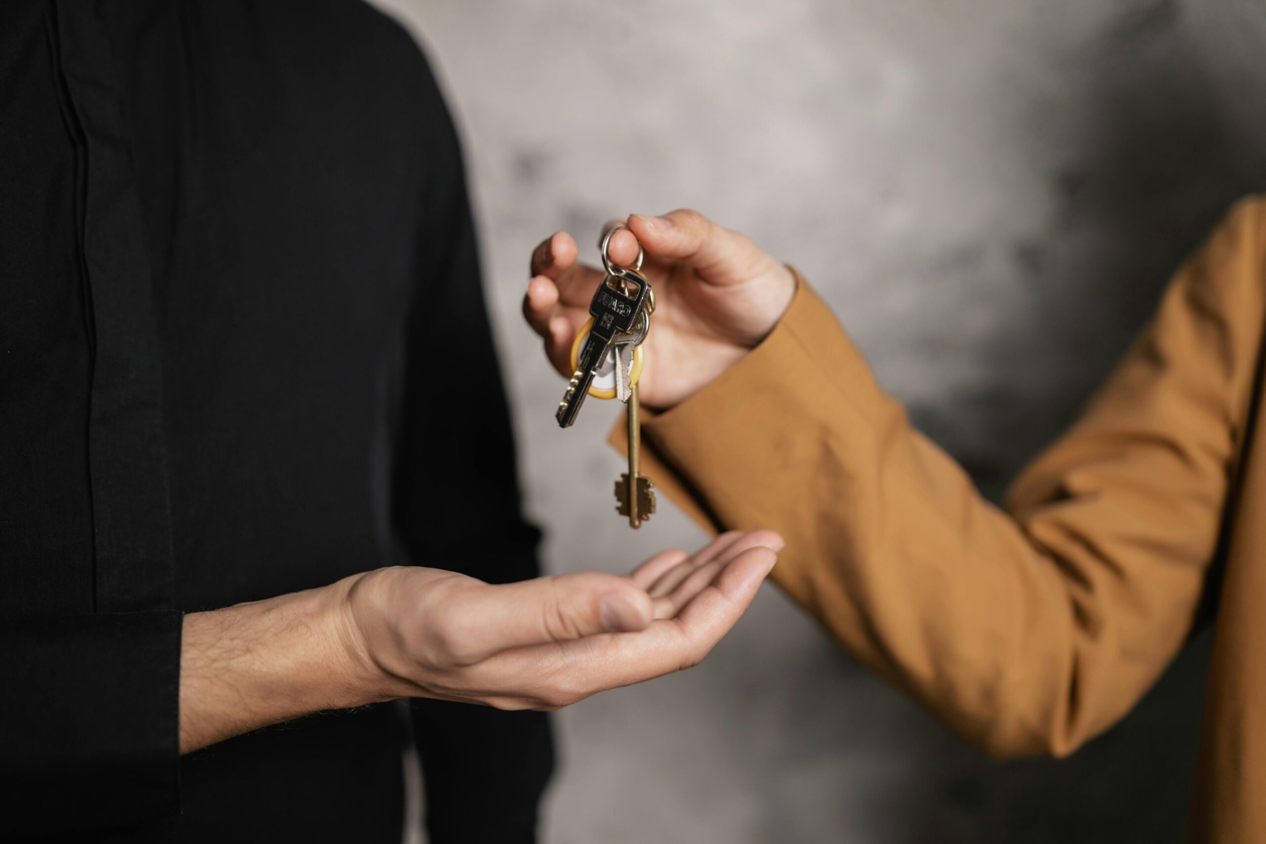 A close-up of a man in a black shirt receiving keys from a real estate agent