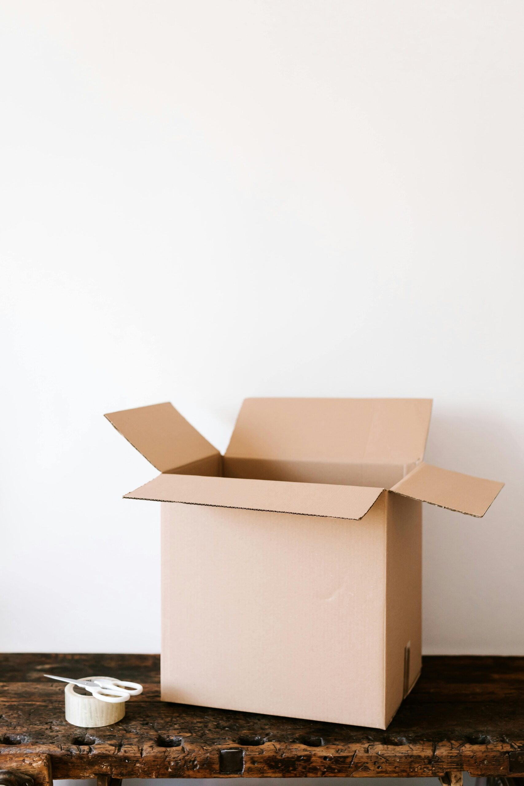 An open brown cardboard box next to a roll of tape and white scissors.