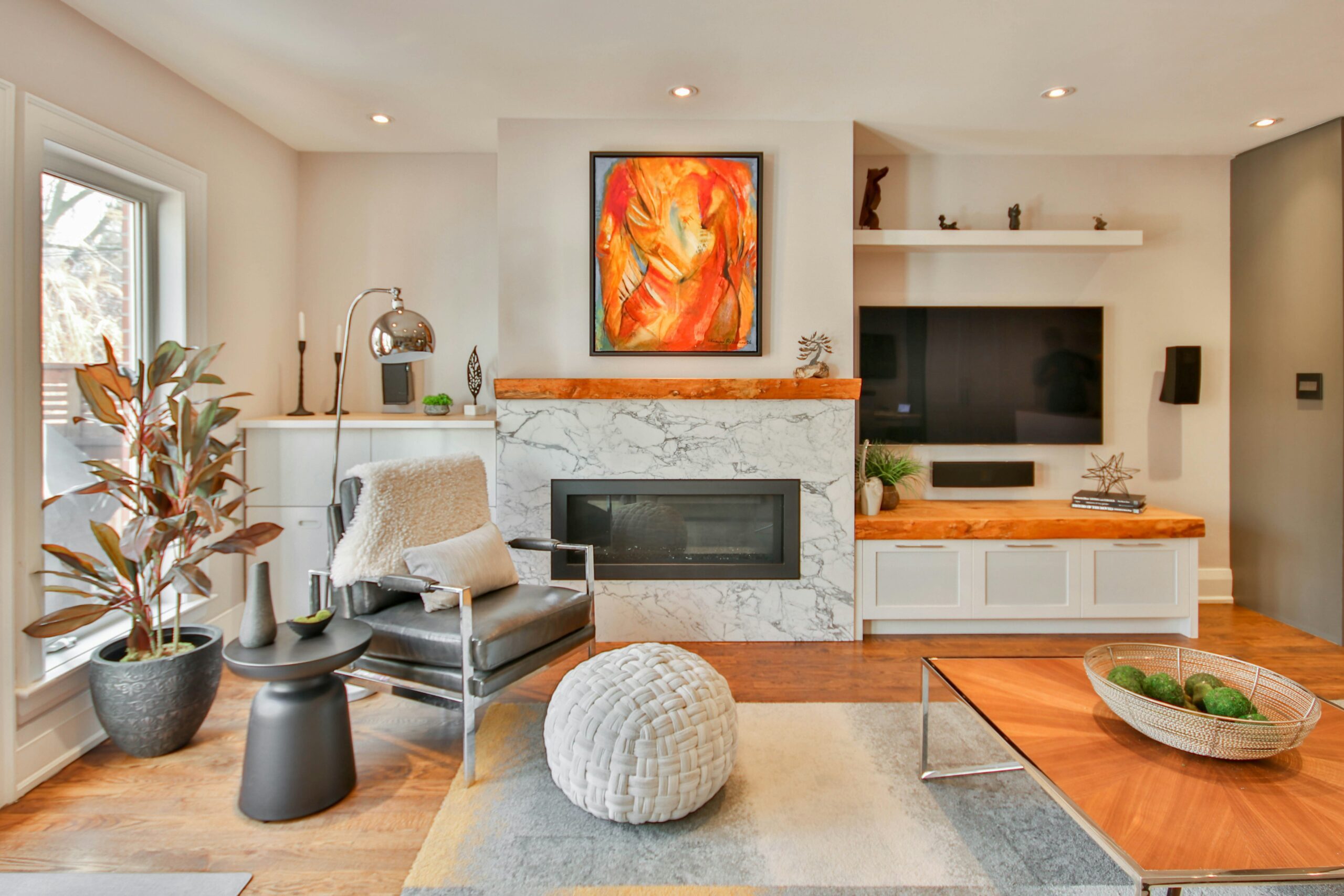 A living room with a modern armchair with metal accents next to a white poof on a hardwood floor.
