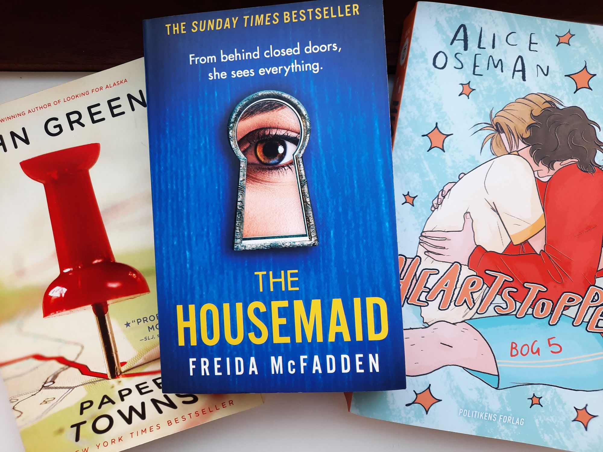 The paperbacks of Paper Towns by John Green, The Housemaid by Freida McFadden, and Heartstopper Volume 5 by Alice Oseman. Reading is a cozy hobby I enjoy