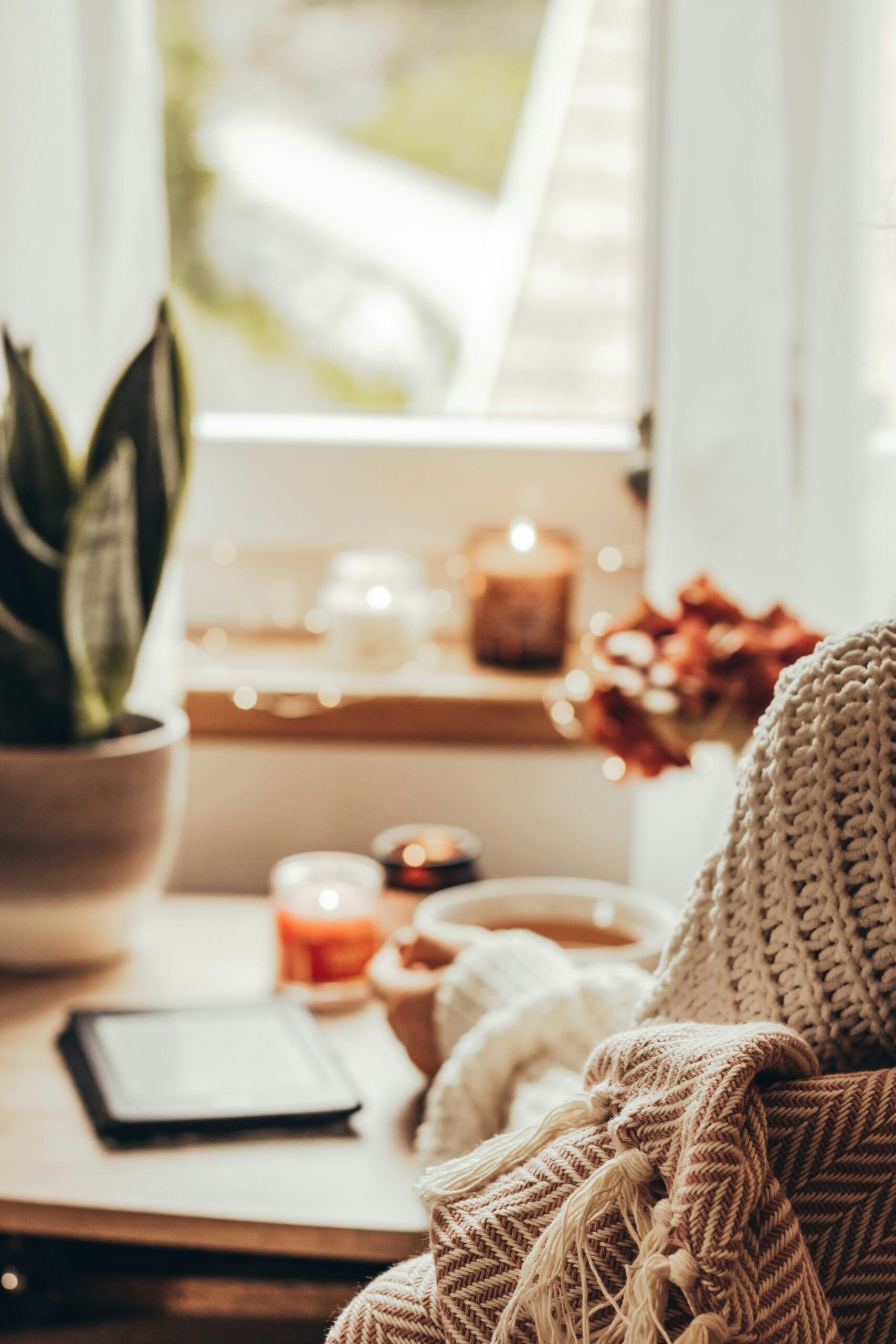 A woman sitting at a desk wearing a white sweater with a woven blanket wrapped around them. In the background are lit candles