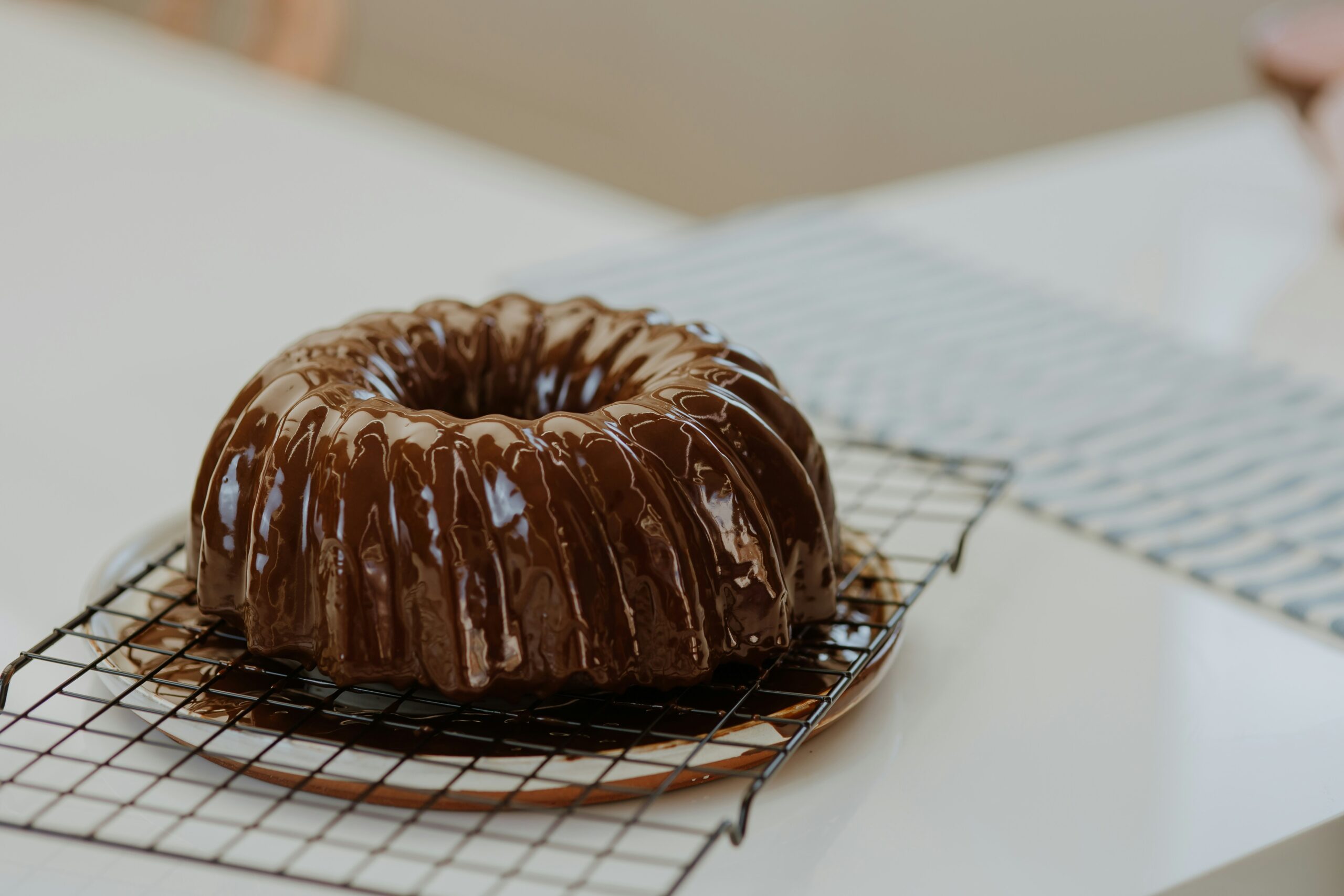 A chocolate bundt cake on a wire cooling rack with melted chocolate poured on it