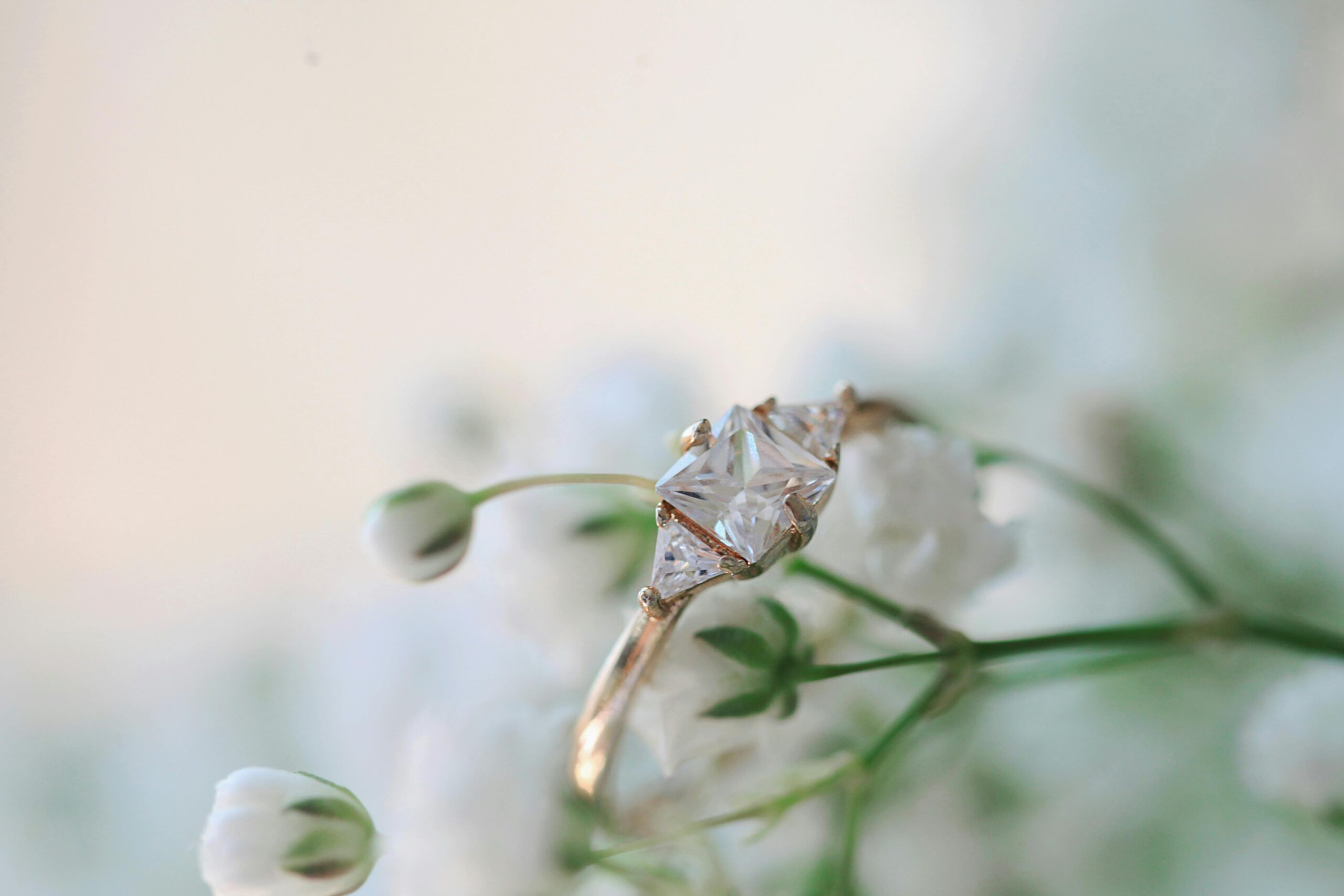 A gold solitaire engagement ring next to white flowers