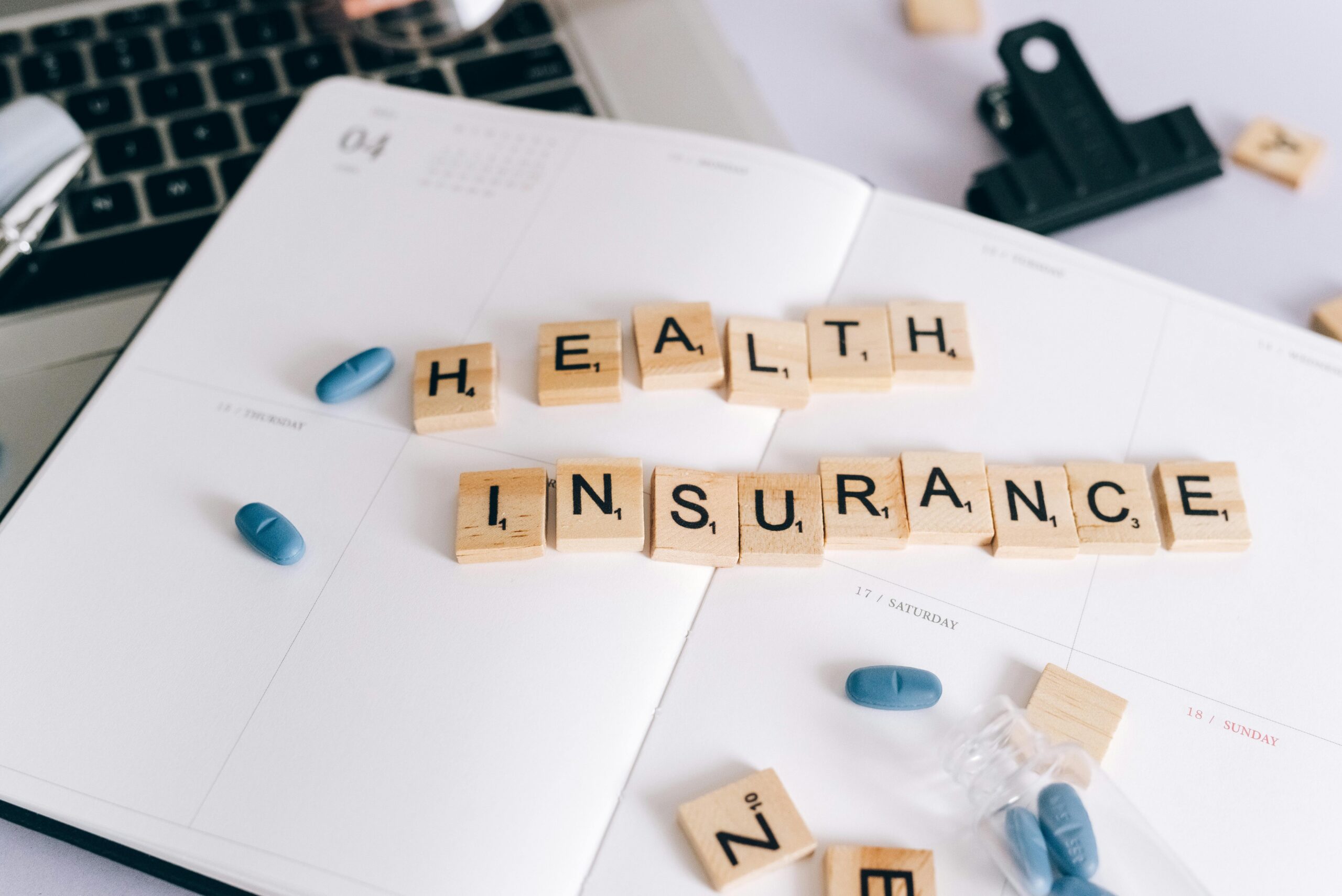 "Health insurance" written in tile letters on top of a planner next to a bottle of pills