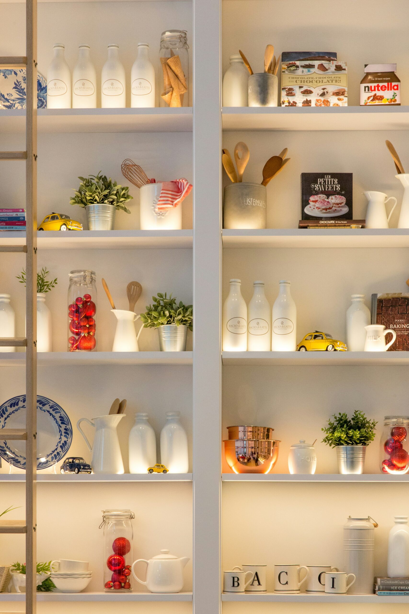 White ceramic bottles, cooking utensils, and cookbooks on a shelf in a kitchen