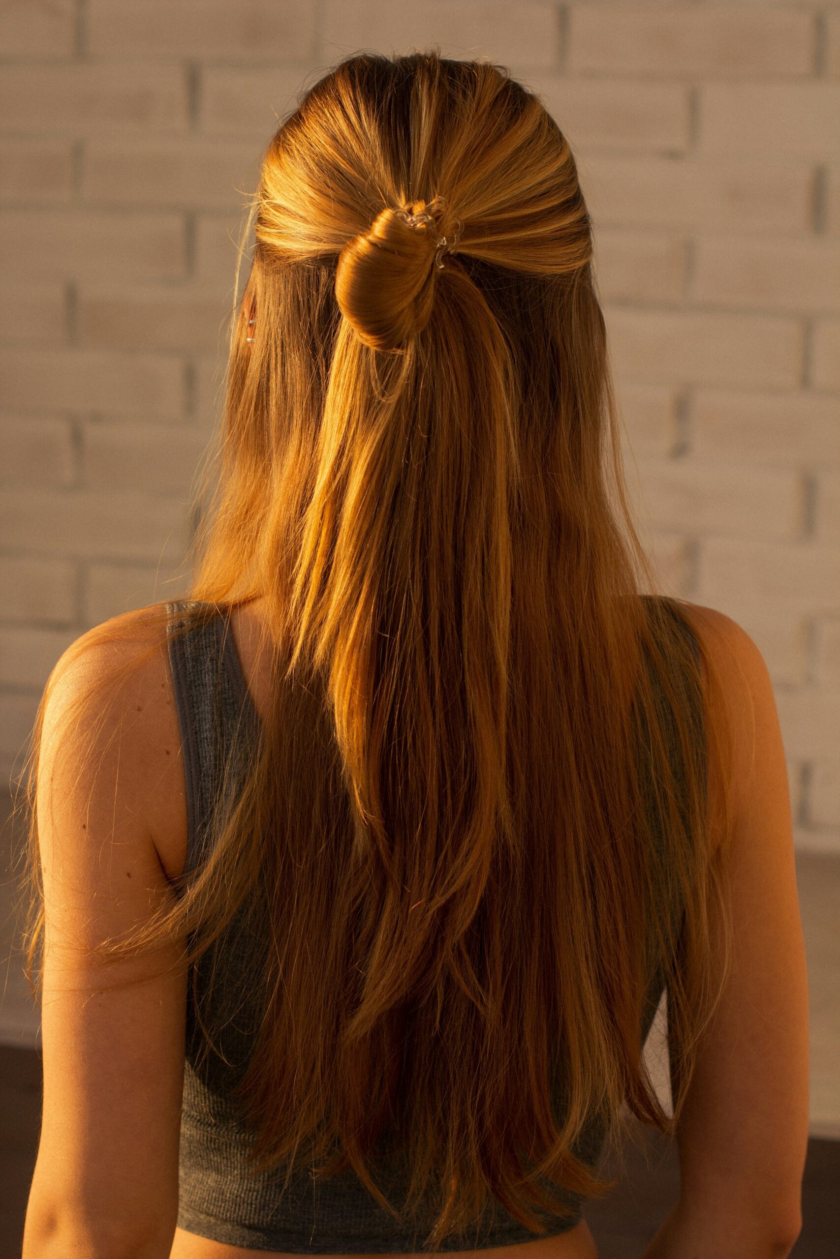 A woman with blonde hair and her back to the camera and showing off her half-up, half-down hairstyle 