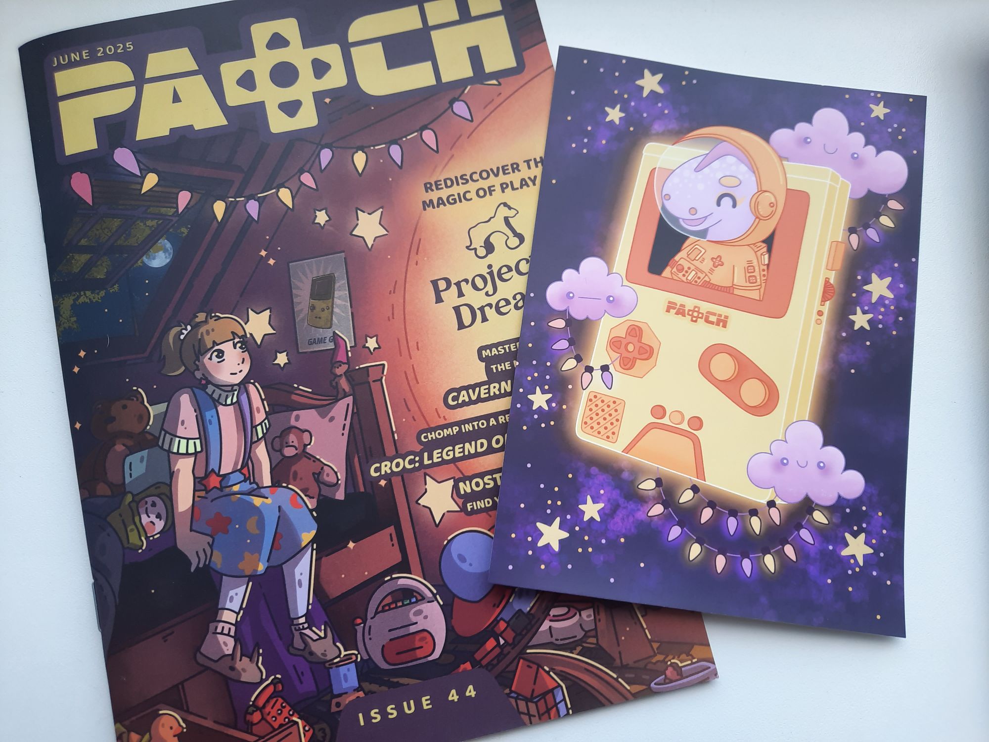 The June 2025 issue of Patch with the game Projected Dreams on the cover. Beside the magazine, is the bonus gift with the level 3 description of the retro gaming art print