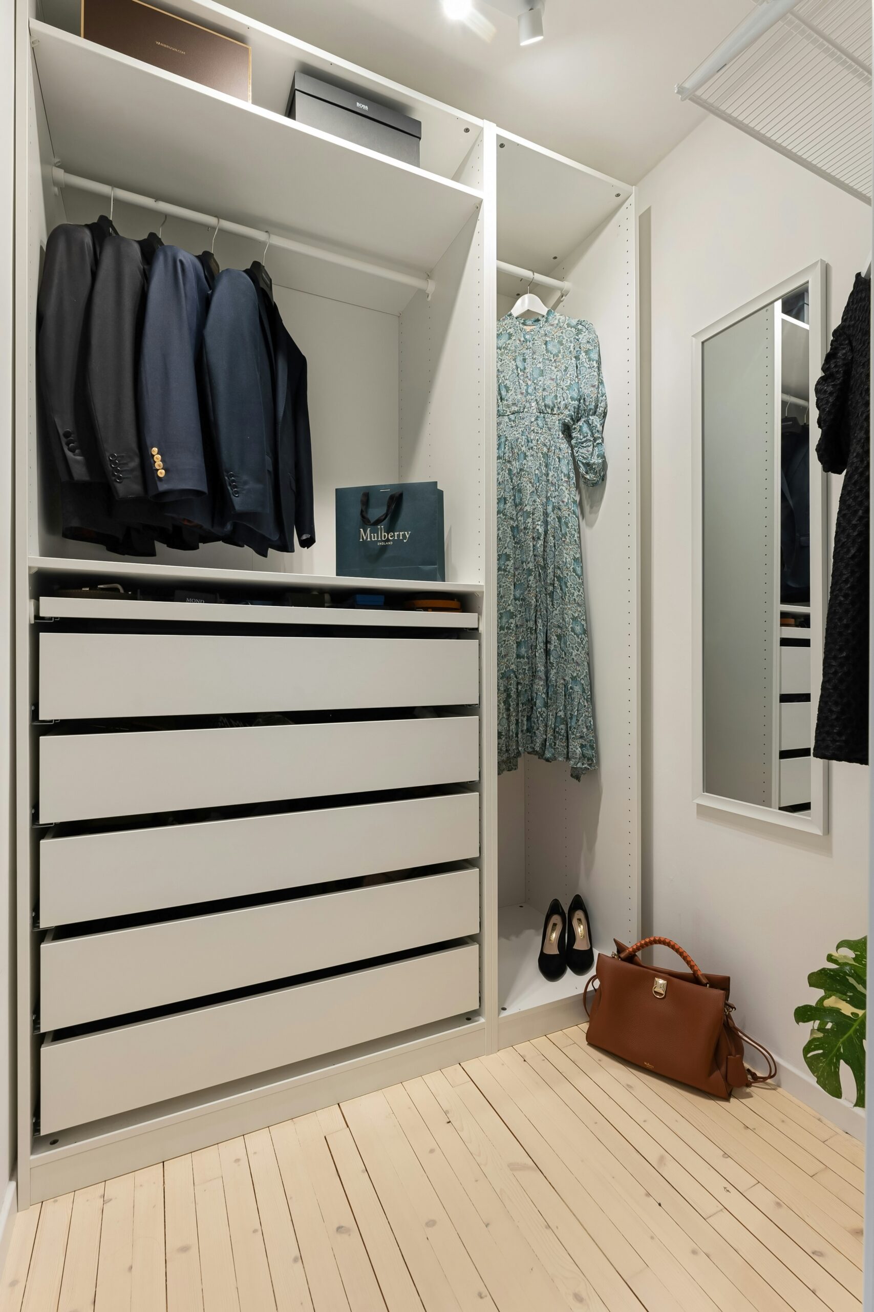 A small closet with suit jackets and dress on hangers and drawers underneath