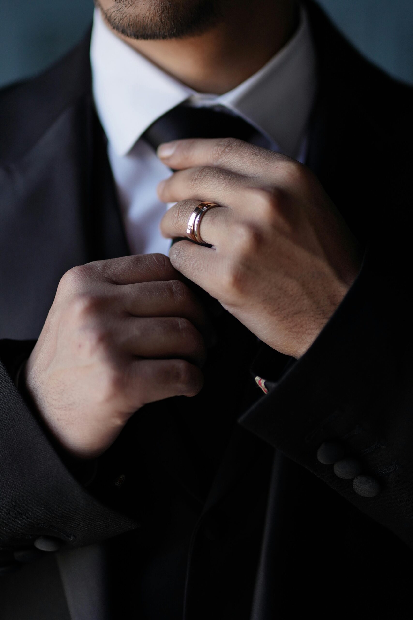 A closeup of a man wearing a wedding ring and fixing his tie