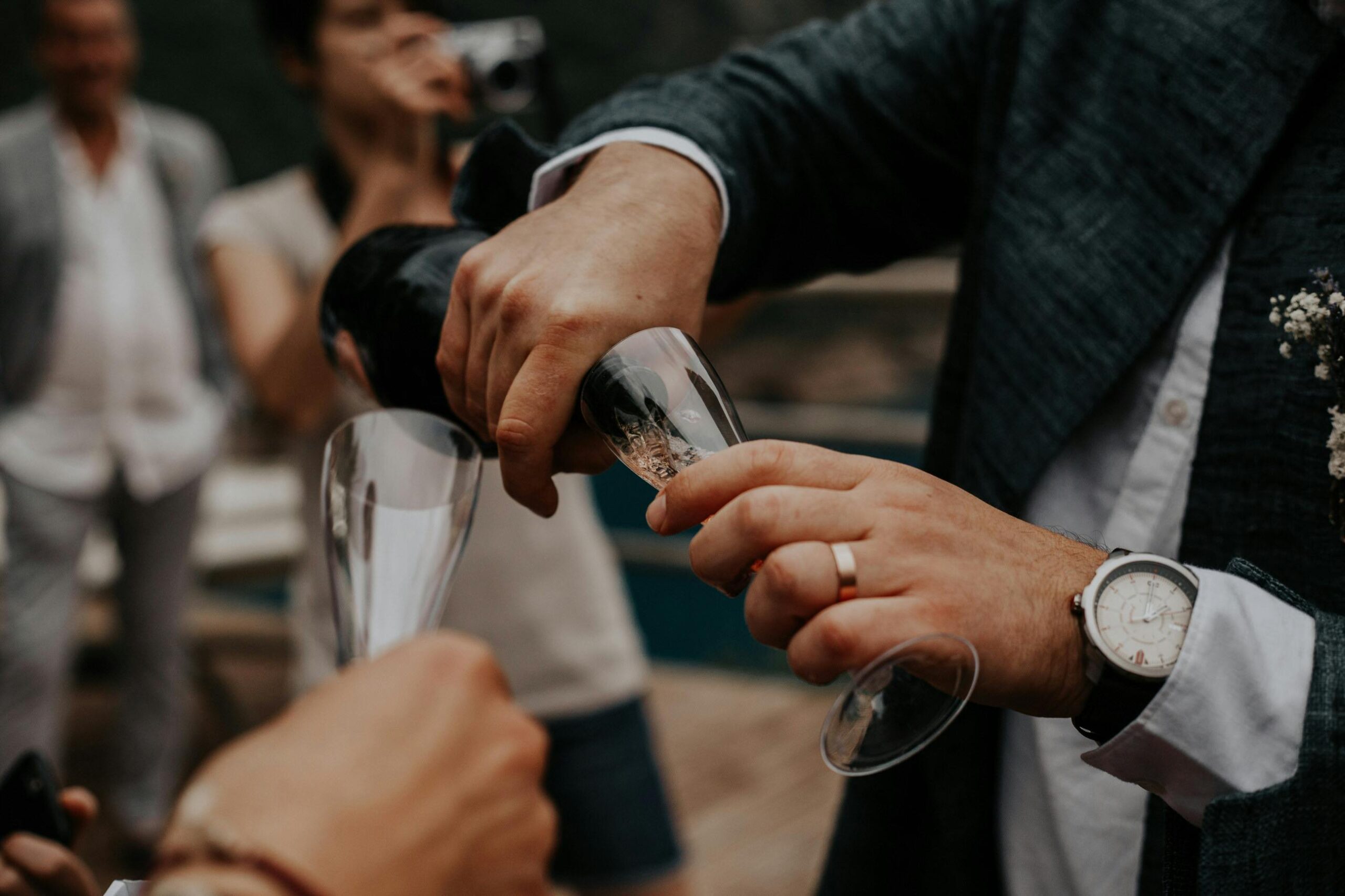 A closeup of a man wearing a wedding ring and pouring a glass of champagne