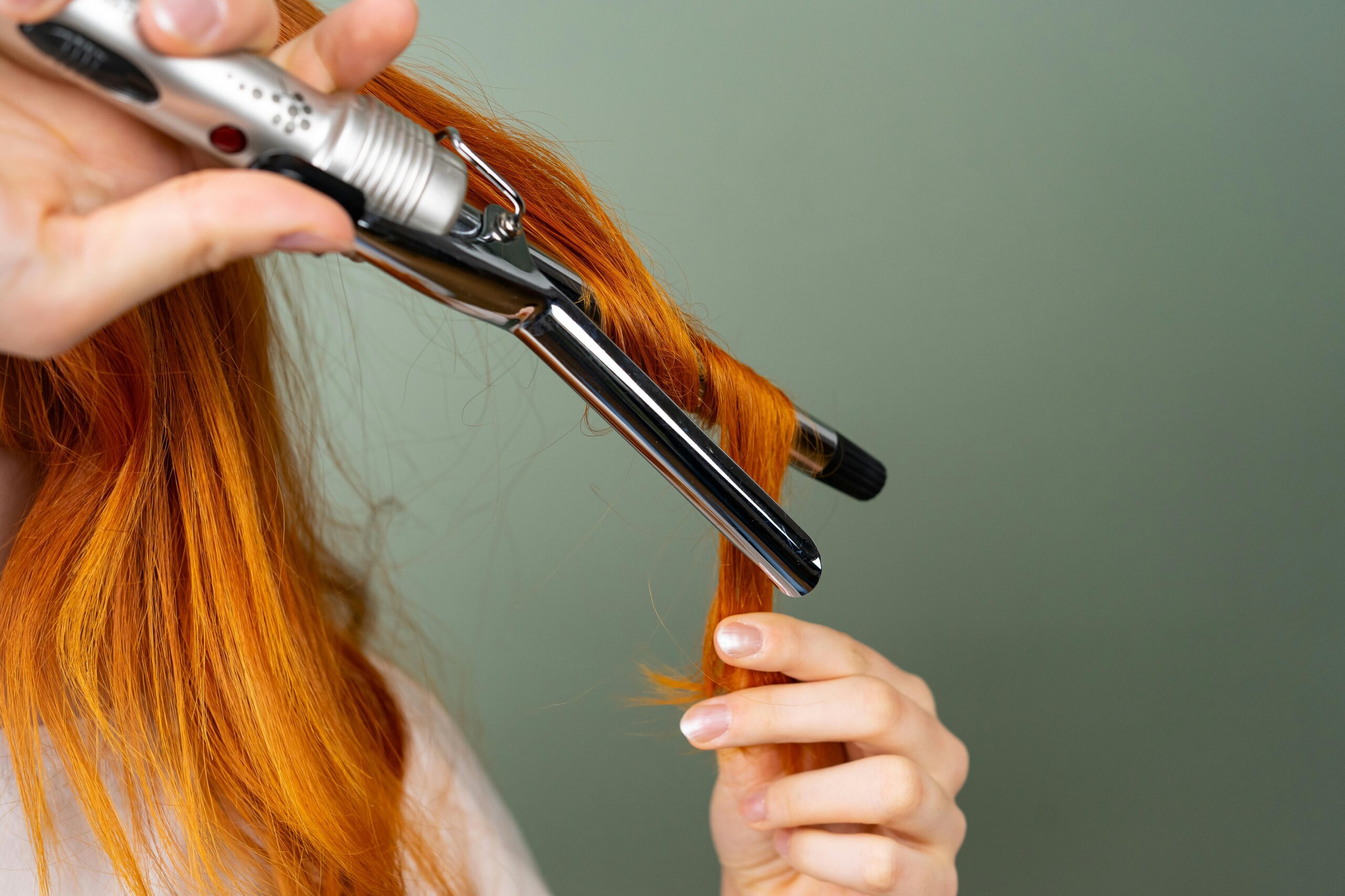 A close up of a woman with red hair using a curling wand