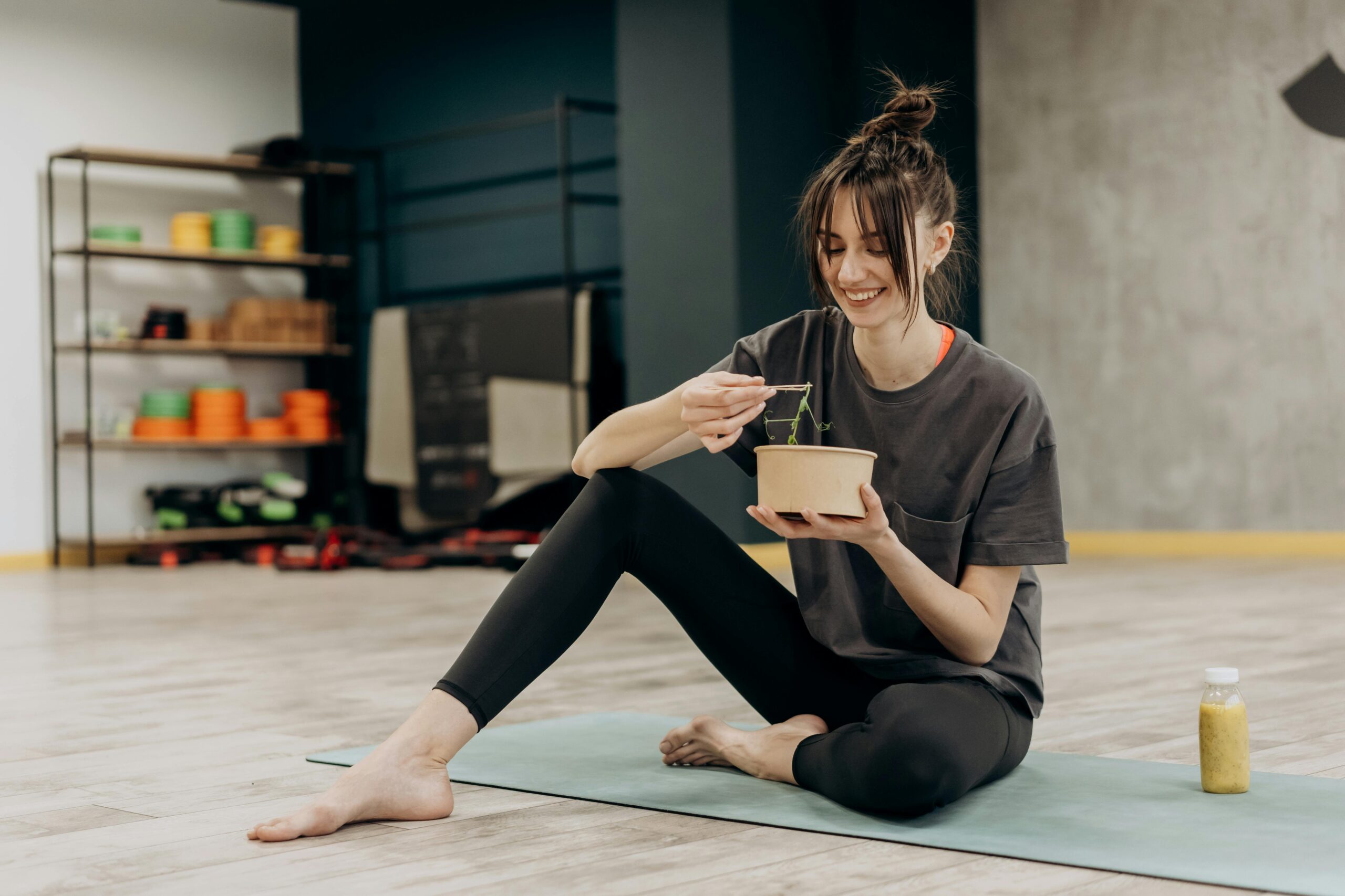A woman wearing black activewear and sitting on a yoga mat and eating a meal