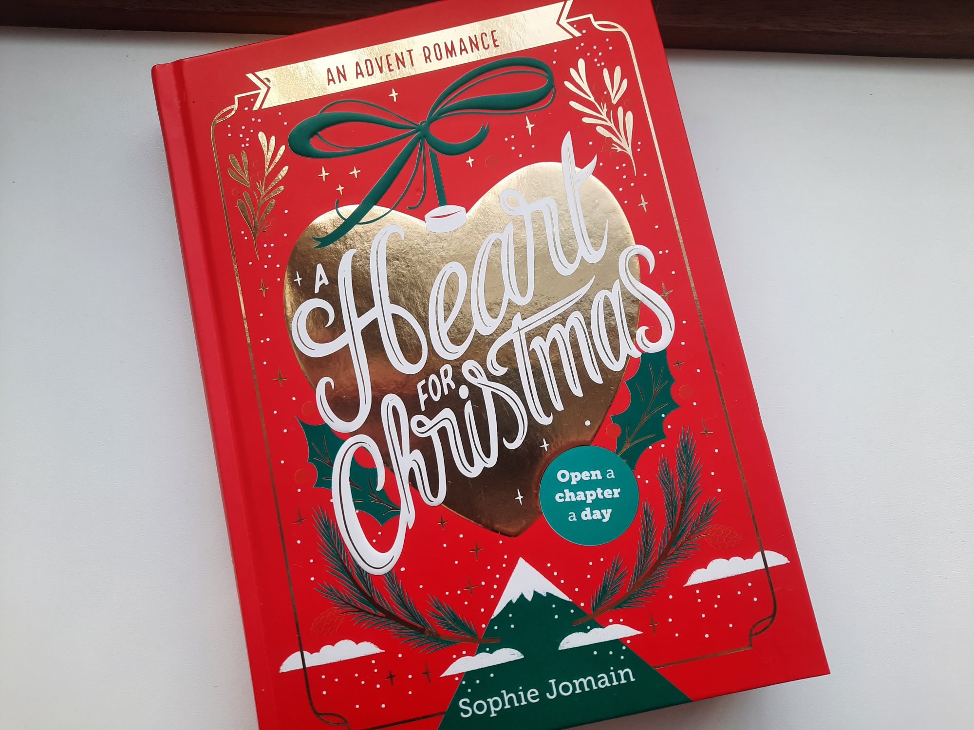 The cover of A Heart for Christmas by Sophie Jomain with a gold heart-shaped ornament above an illustration of a mountain topped with snow