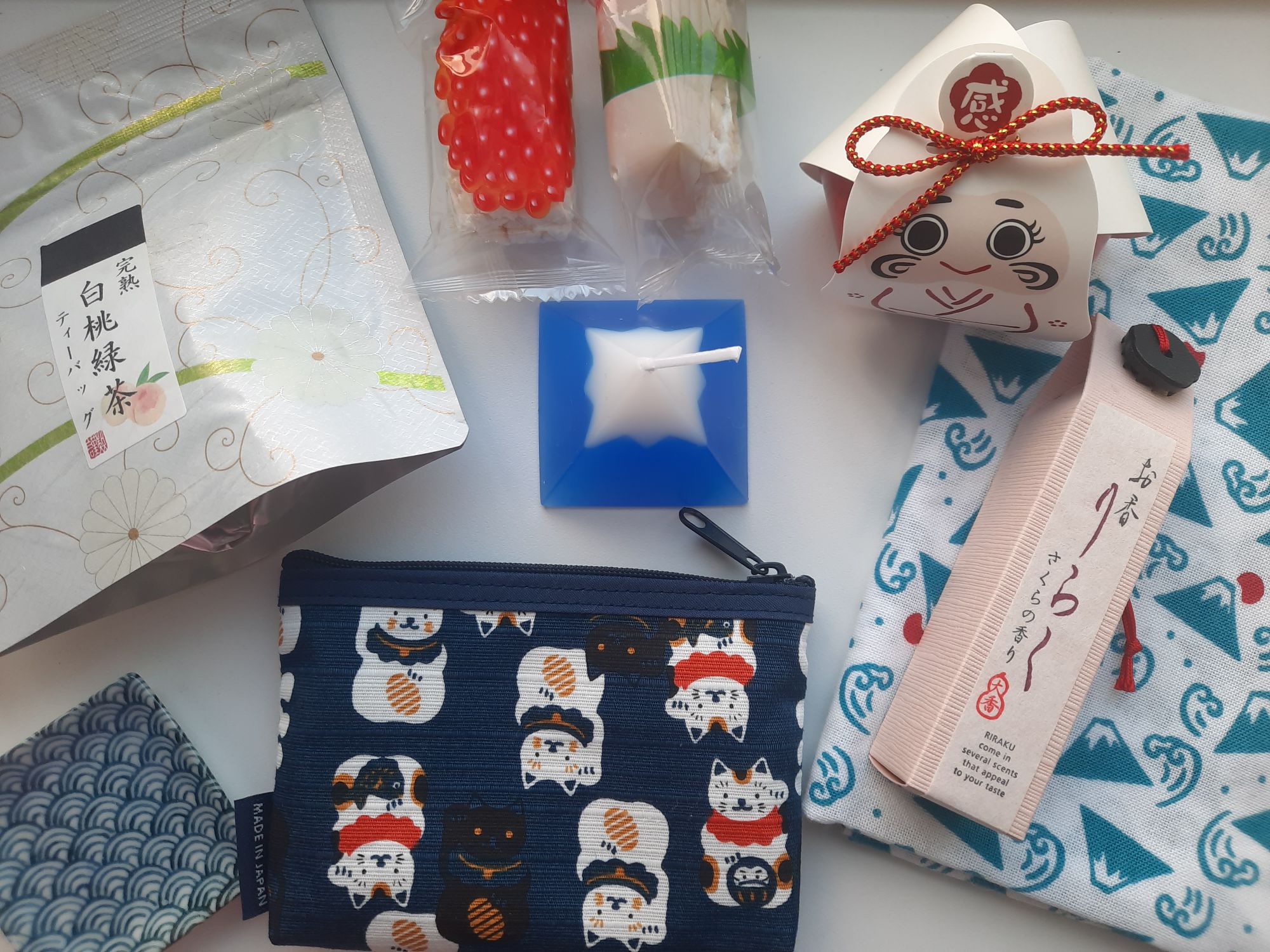 The peach tea, puffed rice snacks, daruma candy, mount fuji patterned tenugui, incense,  Mount Fuji candle, maneki neko pouch, and small plate from the Sakuraco Onsen Retreat Advent Calendar